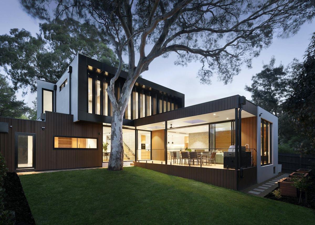 A modern home lit up at dusk, seen from the garden